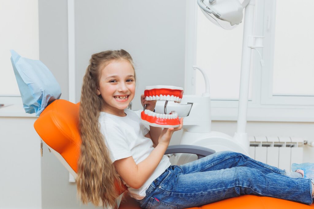little-girl-sitting-on-a-dental-chair-holding-a-model-of-jaws-in-a-dental-clinic-.jpg